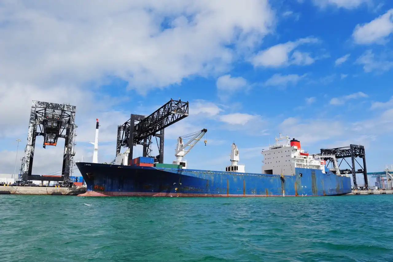 General cargo ship with its own cranes berthed at a terminal with gantry cranes